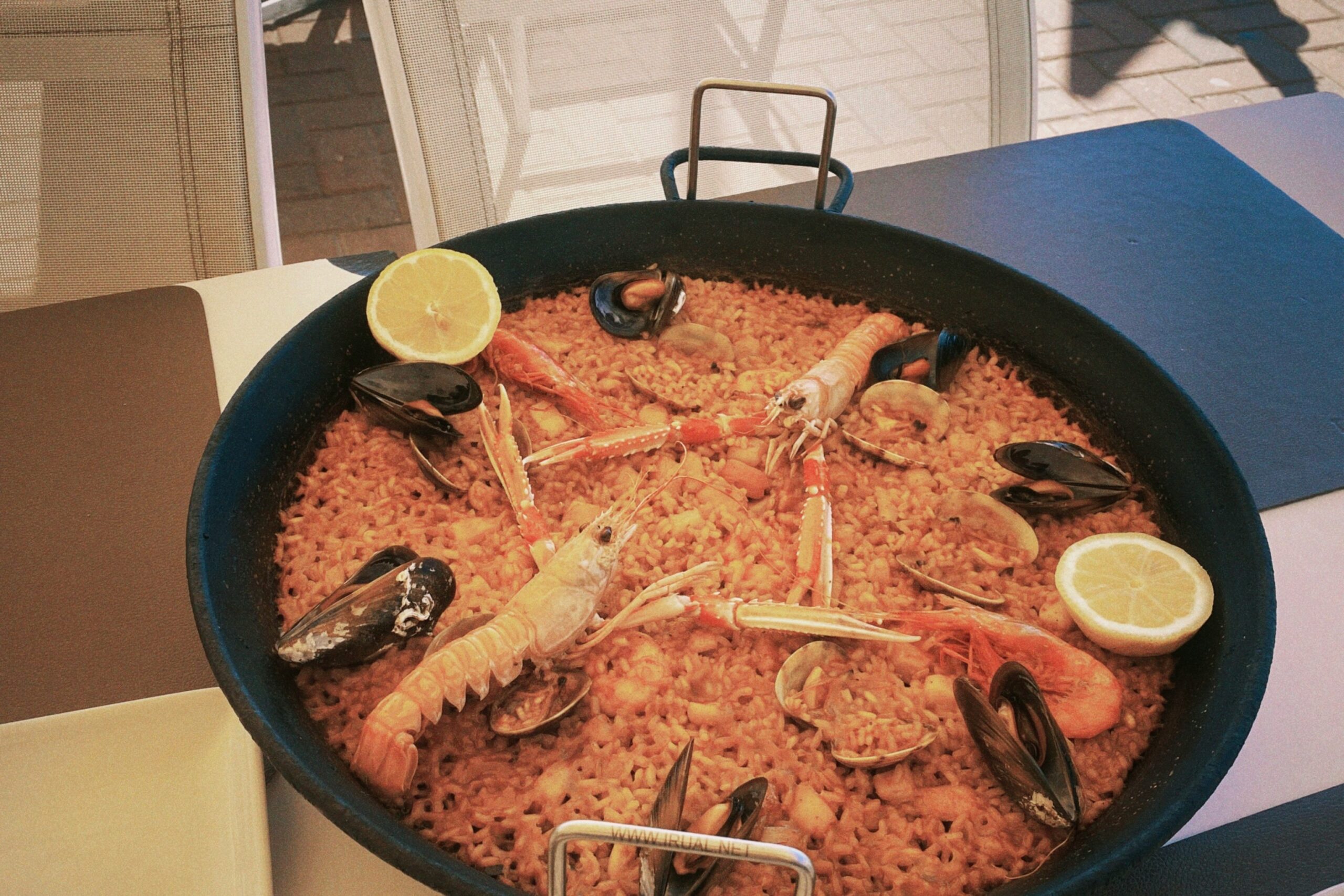 A photo of a paella dish with shrimps and lemons on top of the rice.